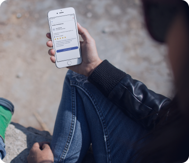 Pessoa sentada ao ar livre segurando um smartphone com o aplicativo indicaz aberto, exibindo a página de avaliação de um prestador de serviços, representando praticidade e usabilidade em qualquer ambiente.